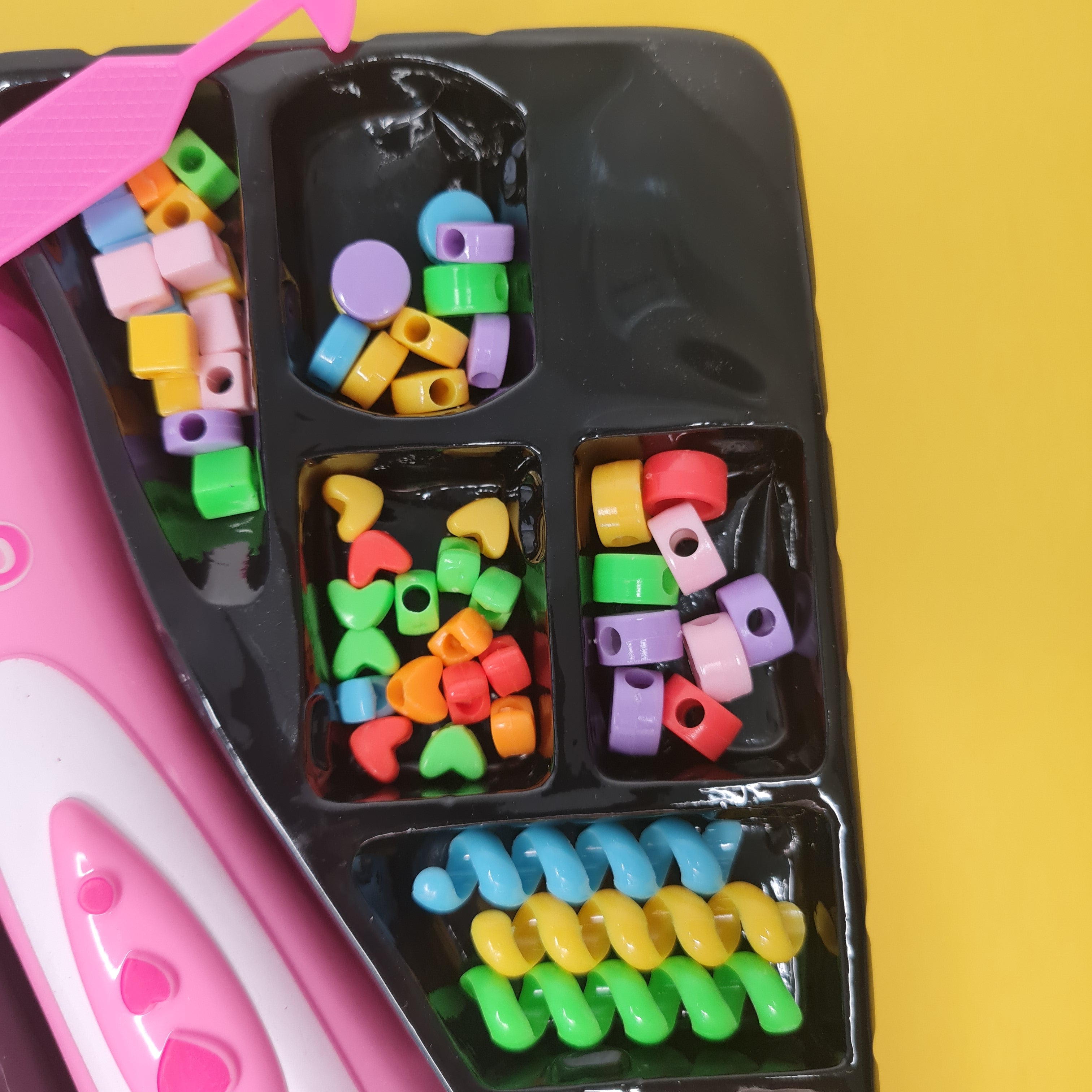 Colorful plastic beads in a compartmentalized container on a yellow background